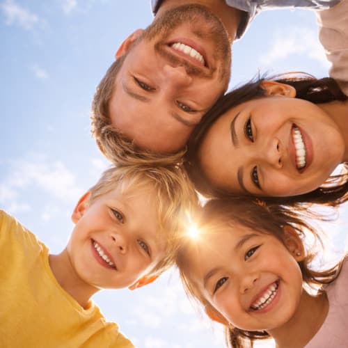 Familienfoto vom Boden aus, das eine Familie mit drei Generationen zeigt, die lächelnd einander umarmen.